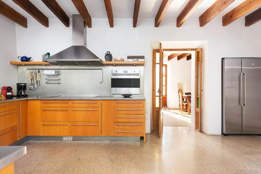 A bright kitchen with orange cabinets, stainless steel appliances, and exposed ceiling beams.