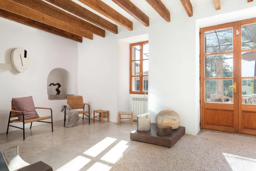 A bright sitting room with exposed wooden ceiling beams and a large wooden-framed window.