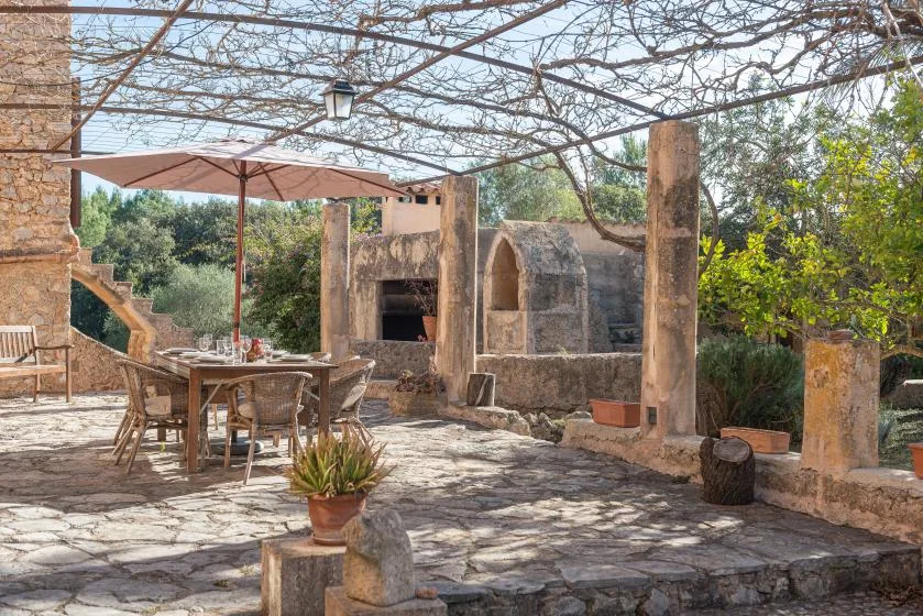 A stone patio with an outdoor dining table beneath a vine-covered pergola.