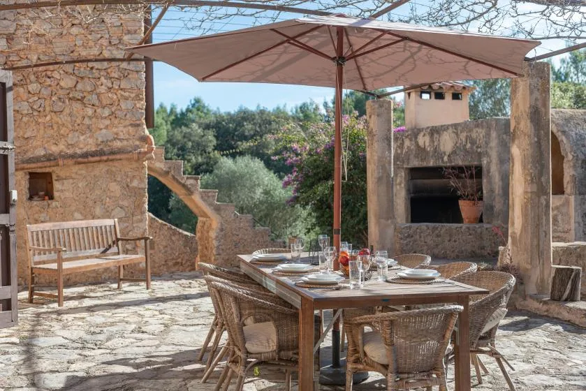 A stone courtyard dining area with a table beneath a large shade umbrella.