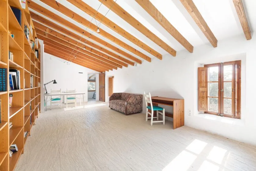 A bright attic room with exposed wooden beams, shelving, and a desk.