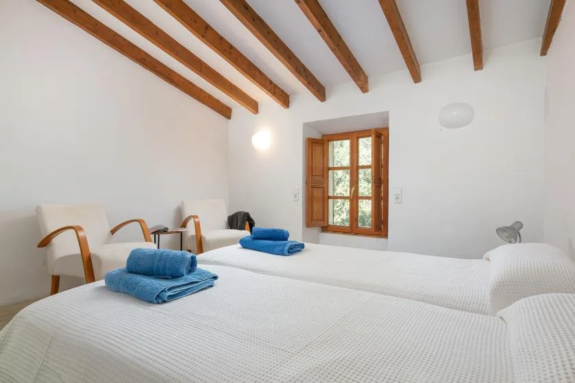 A bright bedroom with two beds and a wooden-framed window.