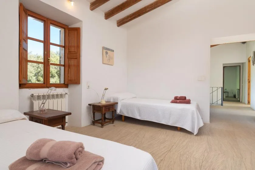 A bedroom with two beds, wooden ceiling beams, and a window with open shutters.