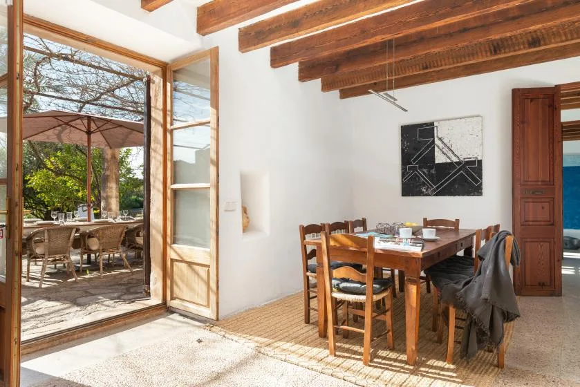 A dining area with a wooden table and chairs beside open doors to a patio.