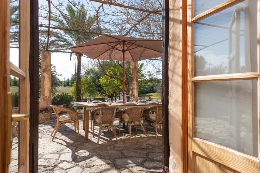 A dining table with seating sits beneath a large umbrella on a stone patio.