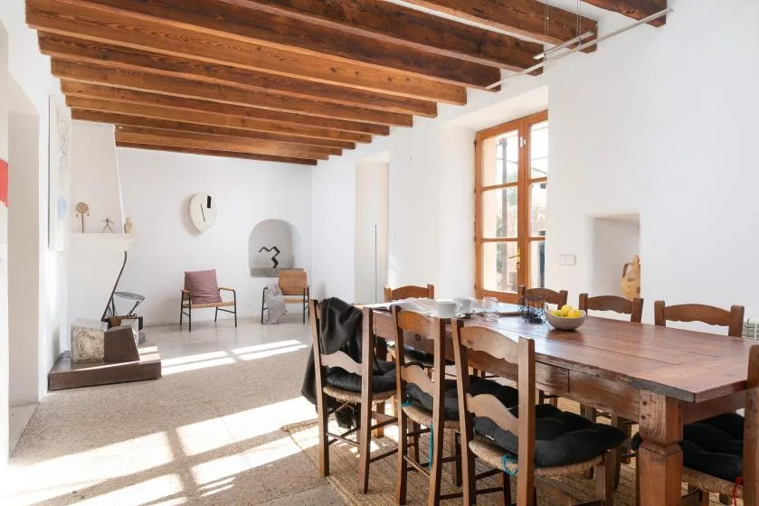 A bright dining area with a long wooden table beneath exposed ceiling beams.