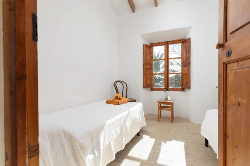 A bright bedroom with two beds and a wooden-framed window.