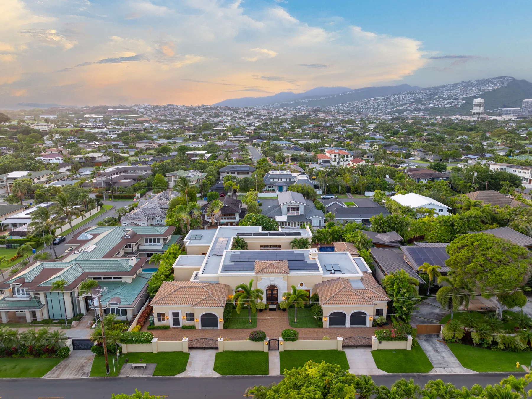 Vista aérea de un vecindario residencial con casas y colinas bajo un cielo colorido al atardecer.