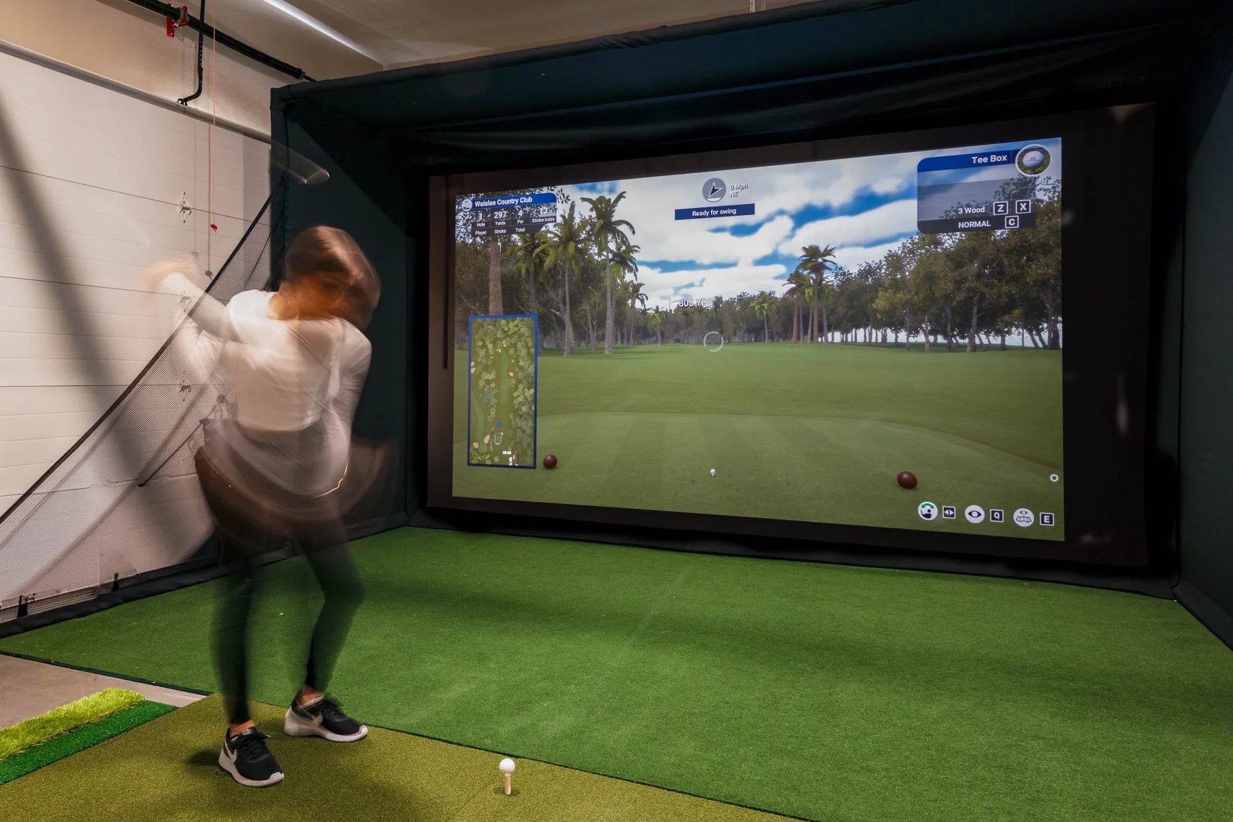 Un simulador de golf interior con una persona golpeando frente a un campo proyectado.