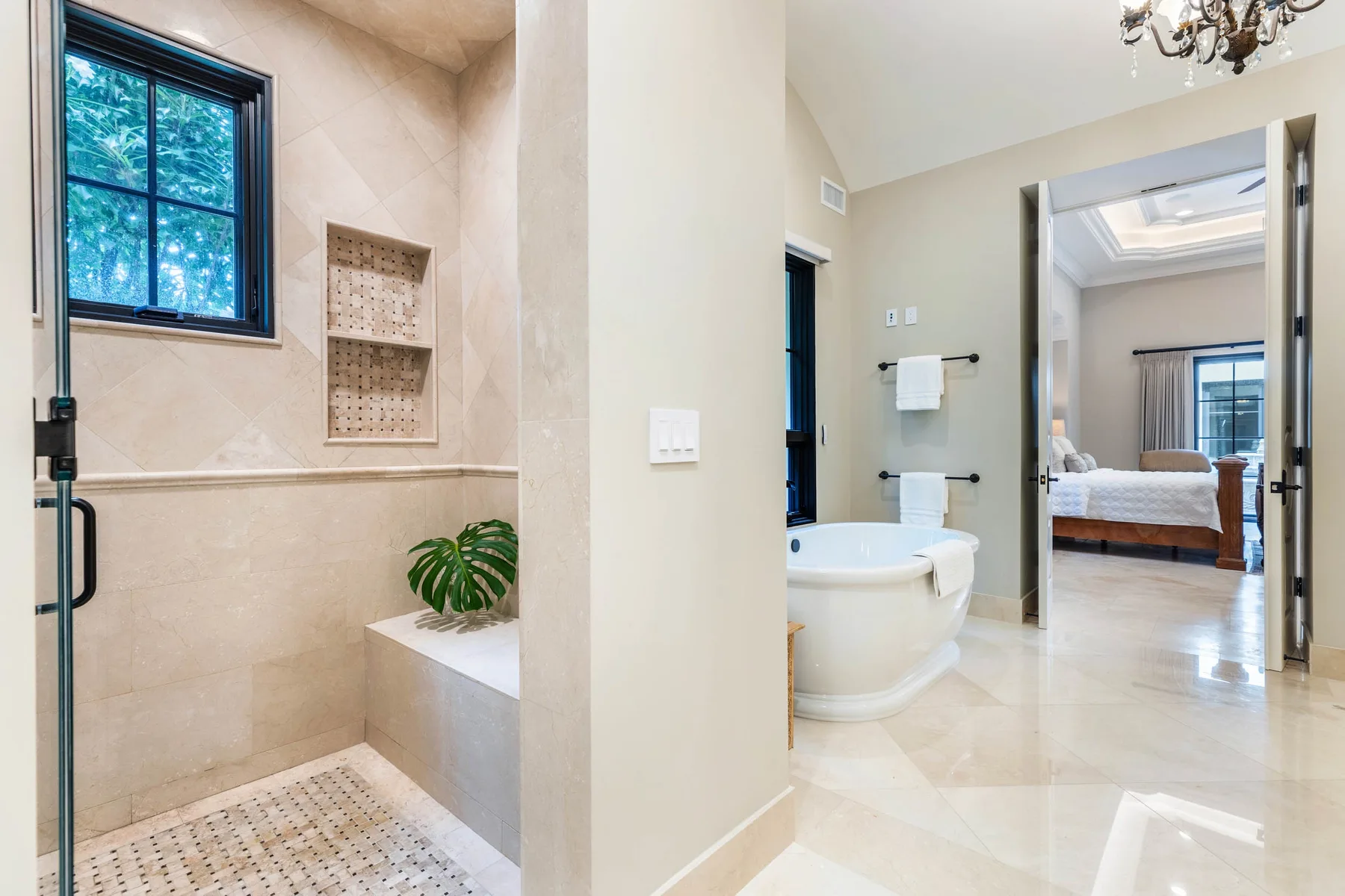 Un baño luminoso con ducha de vidrio, bañera y acceso a un dormitorio.