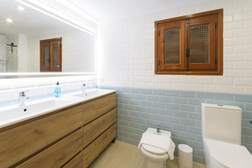 A bathroom with a long sink counter, tiled walls, and wooden window frames.