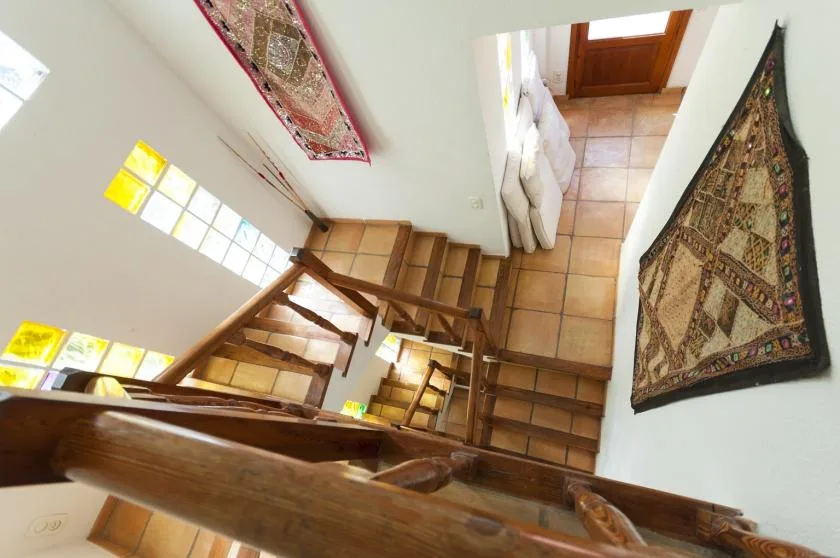 A wooden staircase descends beside tiled flooring and patterned wall rugs.