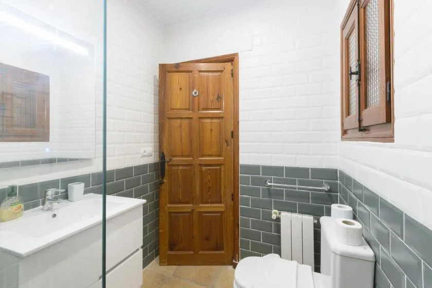 A bathroom with a wooden door, sink, toilet, and gray wall tiles.