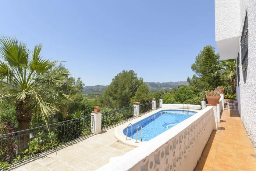 An outdoor swimming pool beside a terrace overlooks green hills.