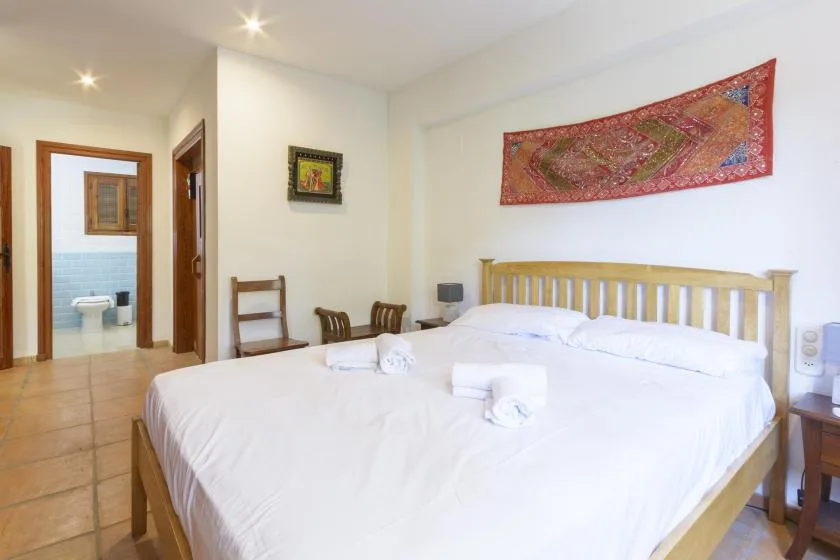 A bright bedroom with a large bed and colorful wall hanging.