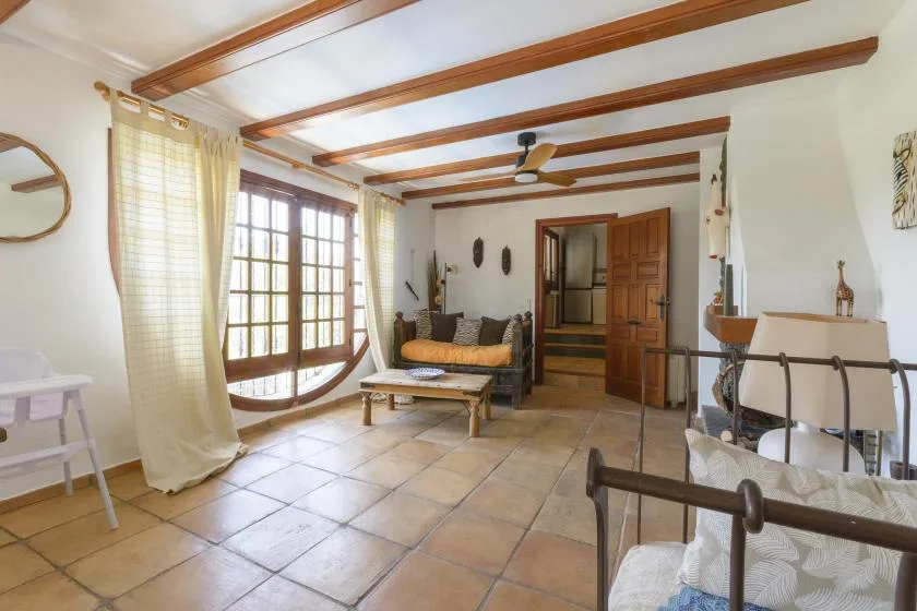 A bright living room with a seating area, large windows, and exposed ceiling beams.