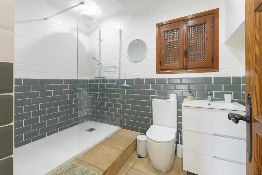 A tiled bathroom with a glass shower, toilet, and sink cabinet.
