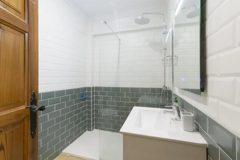 A bathroom with a glass shower, white basin, and gray tiled walls.