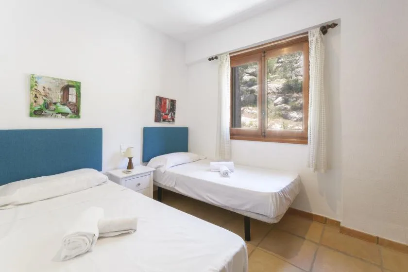 A bright bedroom with two beds and a window overlooking rocky terrain.