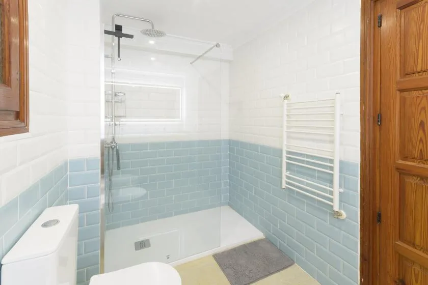A bright tiled bathroom with a shower, bathtub, and wall-mounted towel rail.