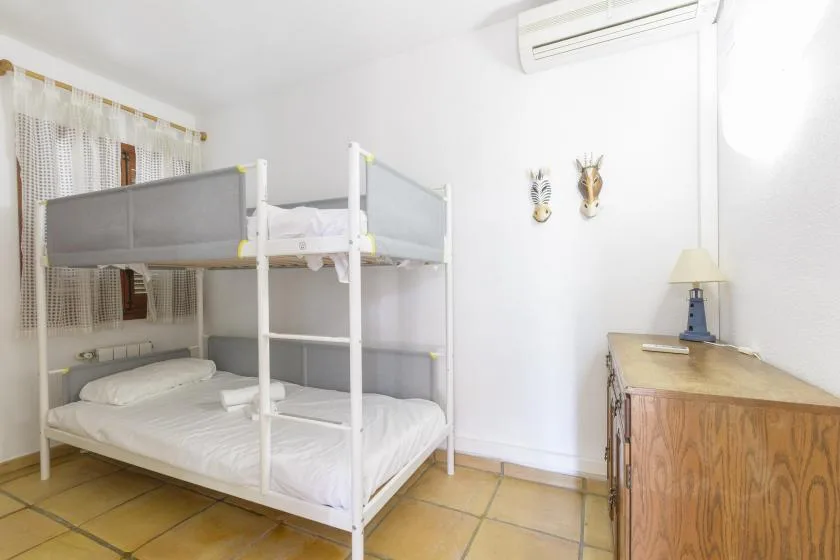 A bright bedroom with bunk beds, a wooden dresser, and a window with curtains.