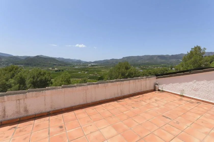 A tiled terrace overlooks green hills beneath a clear blue sky.