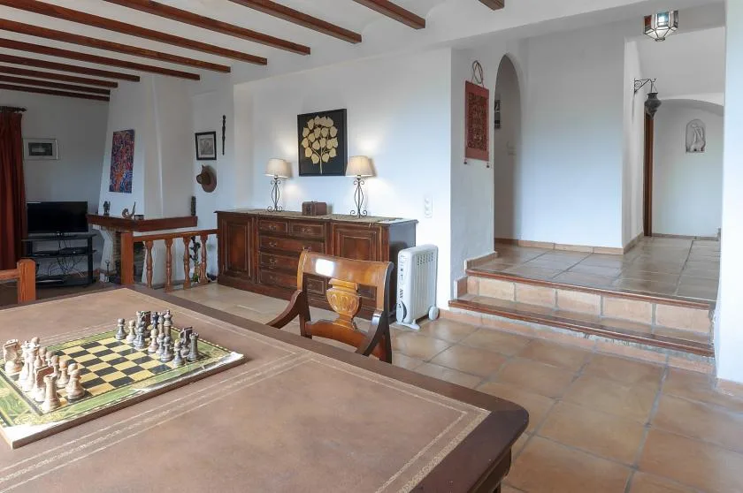 A furnished living room with a chessboard on the table and wooden ceiling beams.