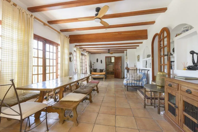 A long dining room with wooden tables, tiled floors, and exposed ceiling beams.