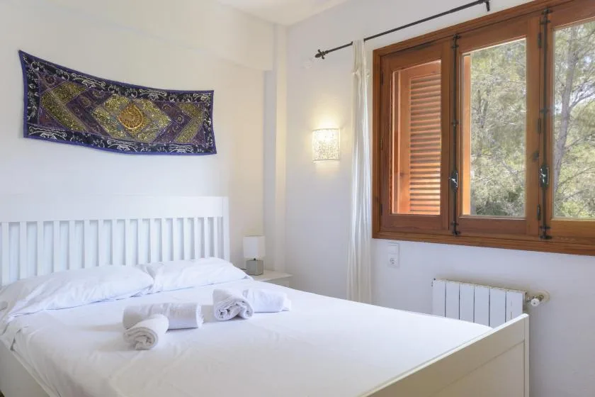 A bright bedroom with a white bed and a large wood-framed window.