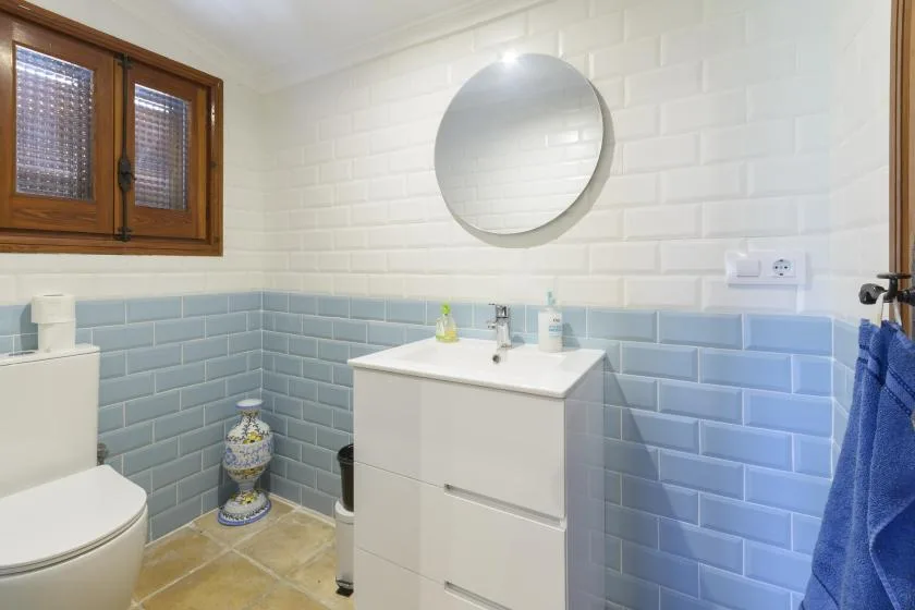 A tiled bathroom with a sink cabinet, round mirror, and toilet.