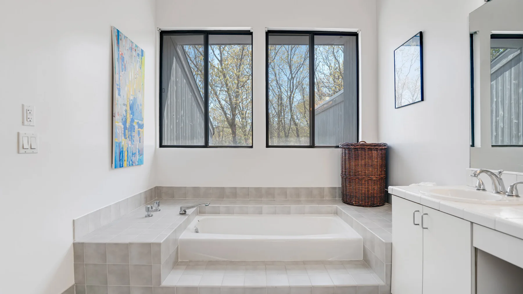 Un baño luminoso con una bañera empotrada bajo dos ventanas.