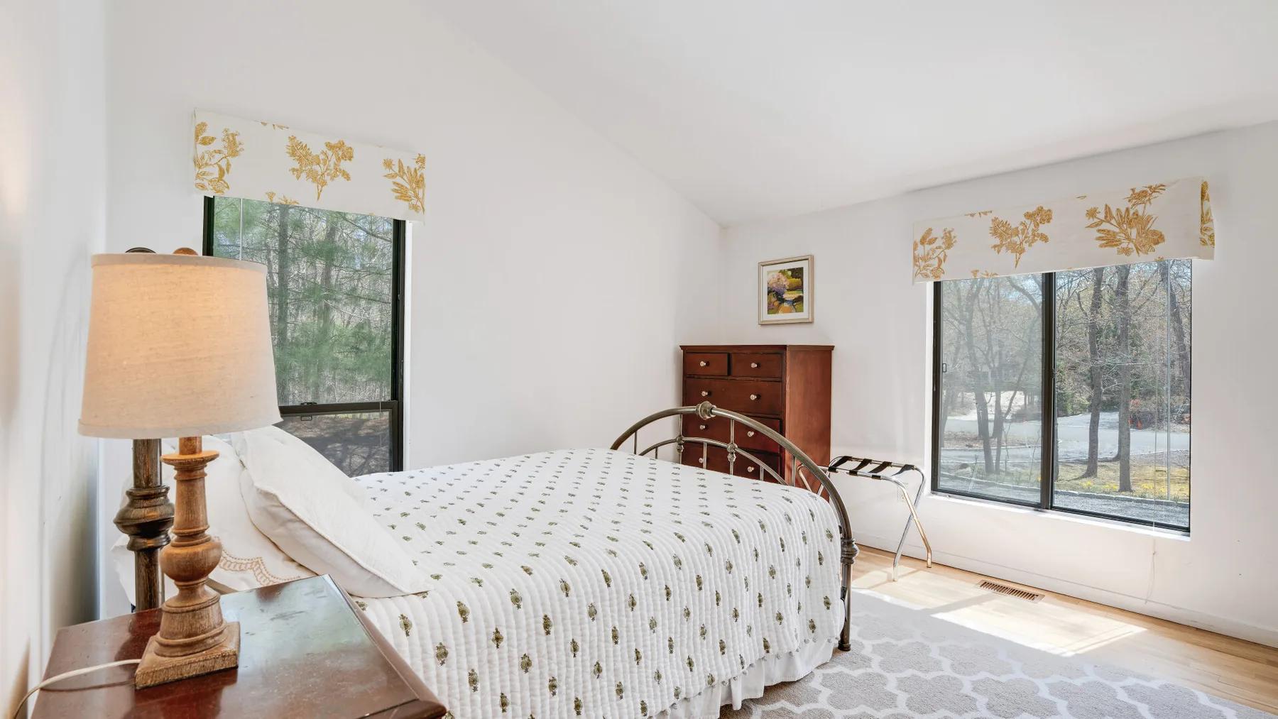 A bright bedroom with a patterned bed and large windows overlooking trees.