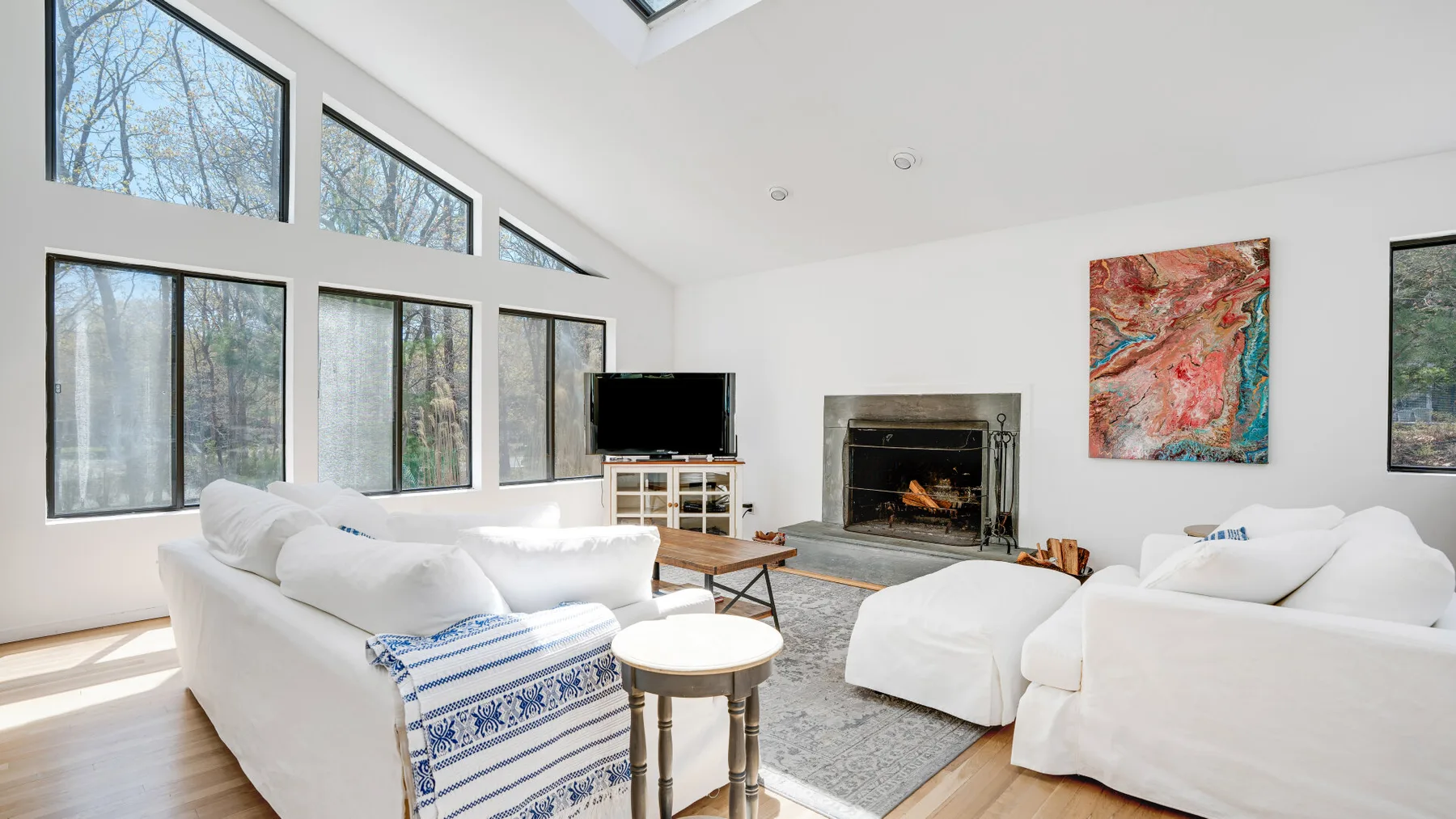 Una sala luminosa con grandes ventanas, asientos blancos y una chimenea.