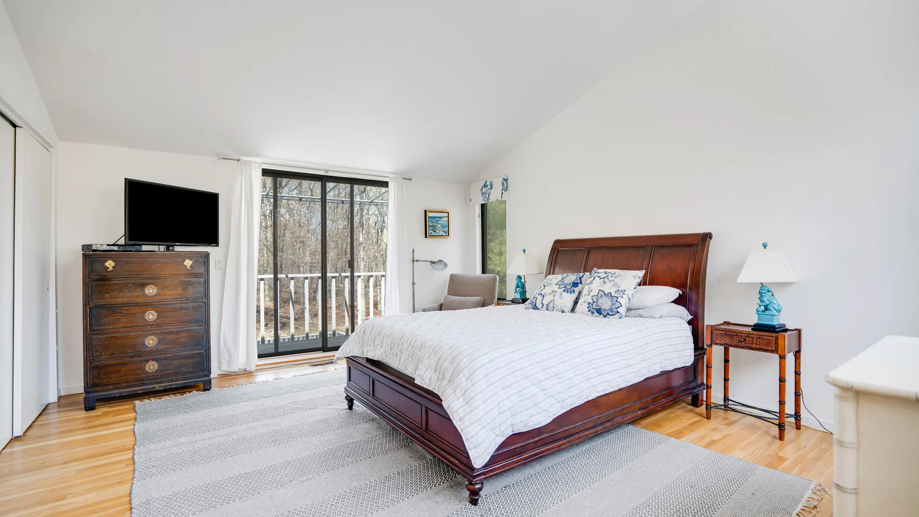 A bright bedroom with a wooden bed and glass doors opening onto a balcony.