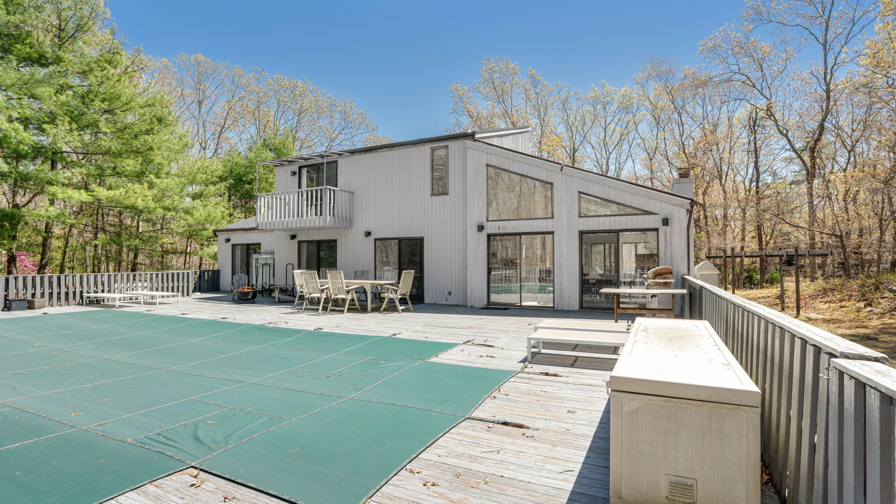 A modern house overlooks a large outdoor deck with a covered pool.