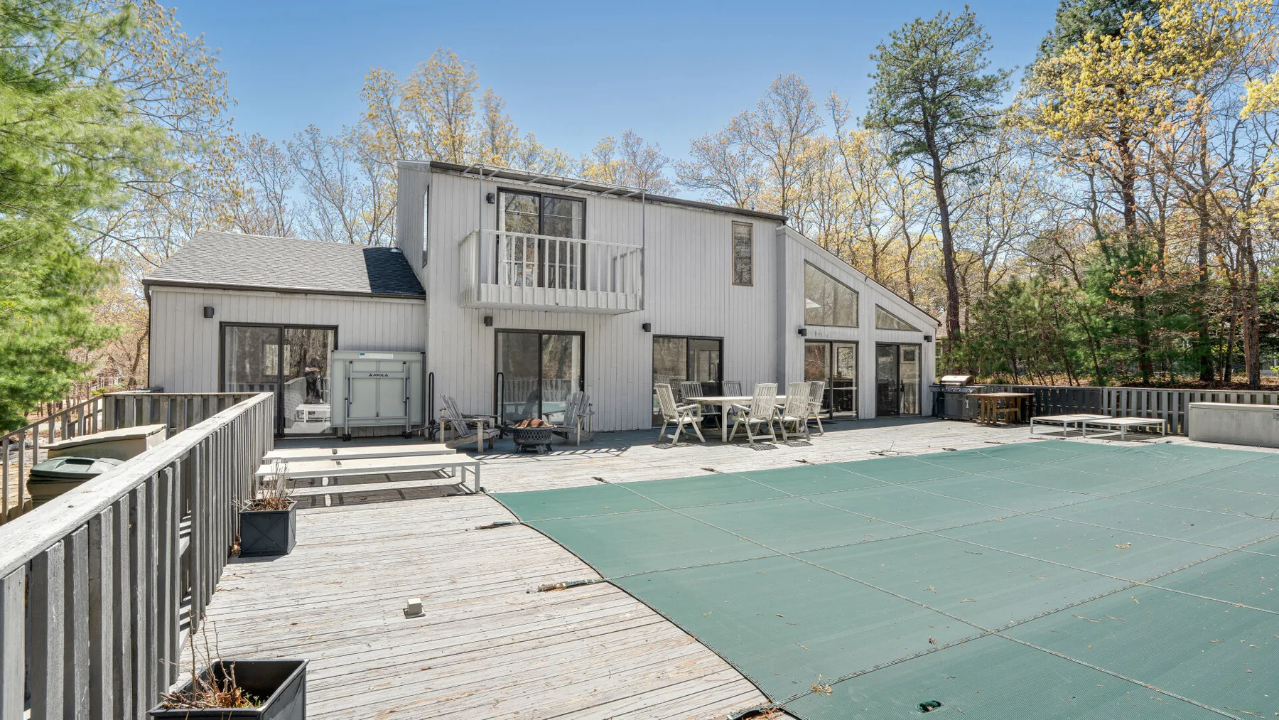 Una casa moderna está junto a una piscina cubierta grande y una terraza de madera.