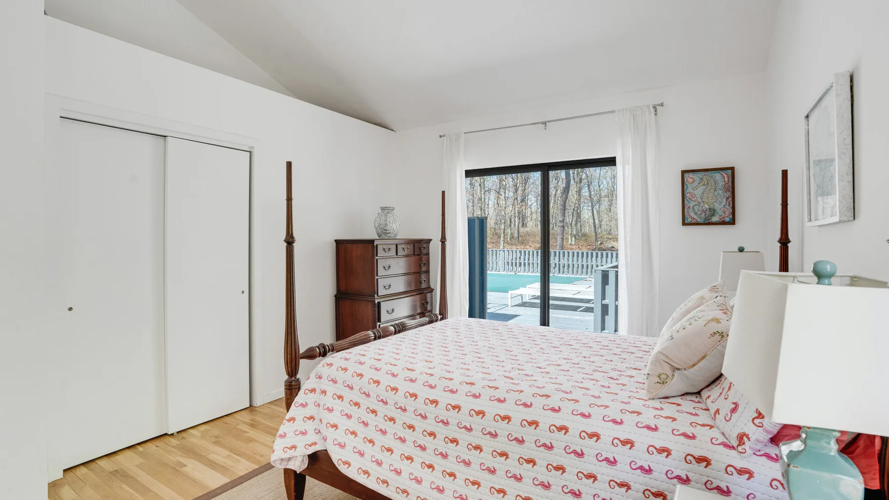 A bright bedroom with a bed beside a large window overlooking trees.