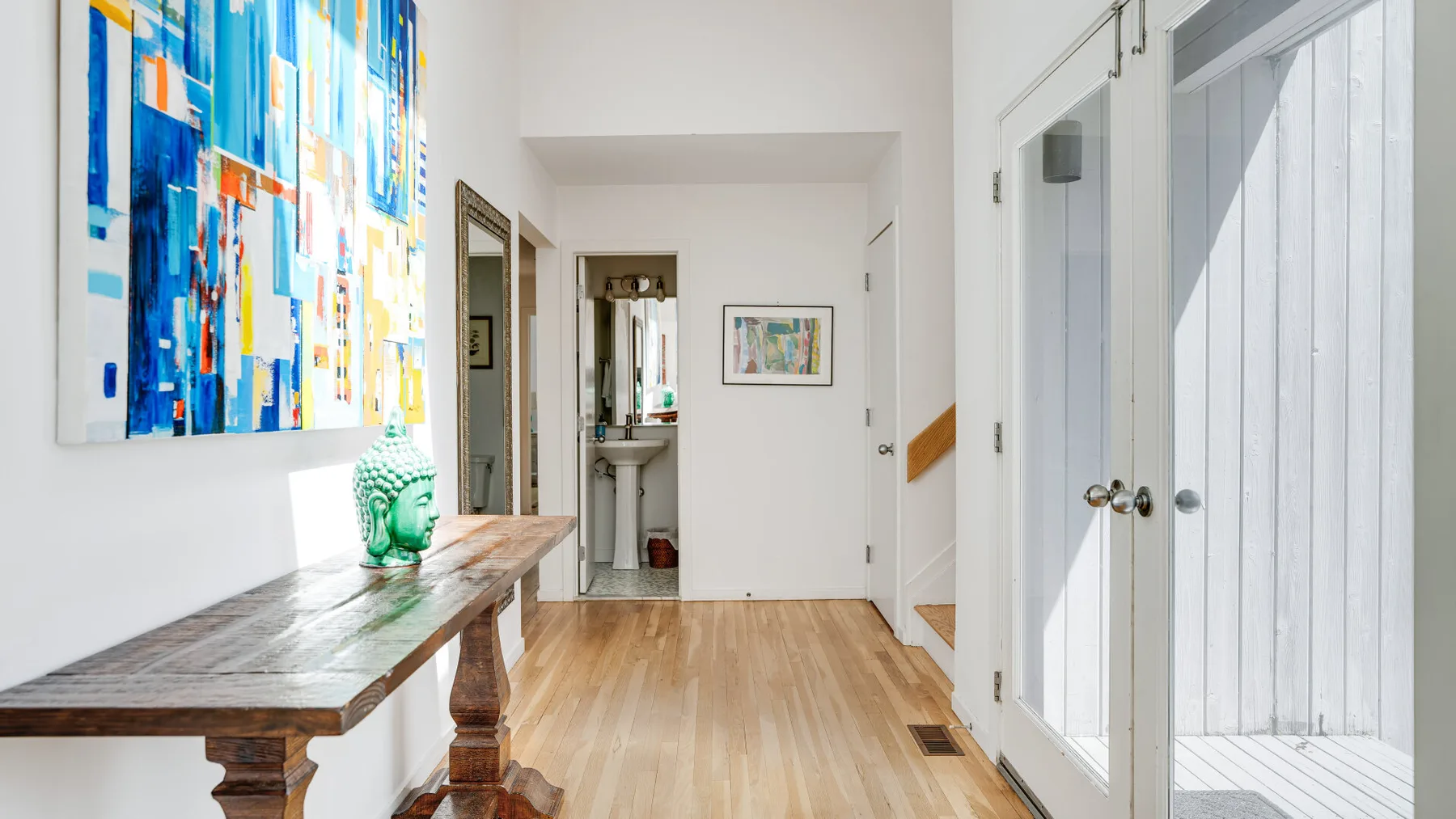 A bright hallway with colorful artwork and a long wooden console table.