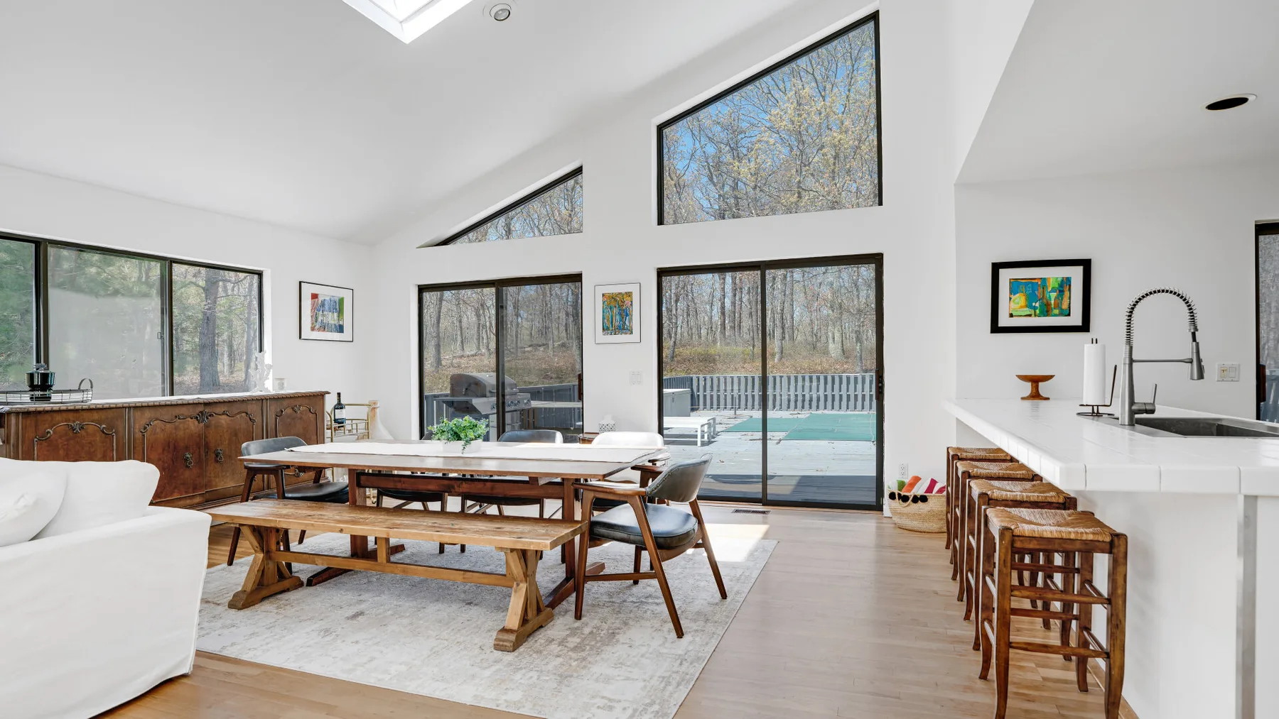 A bright open-plan dining and kitchen area has large windows overlooking a pool.