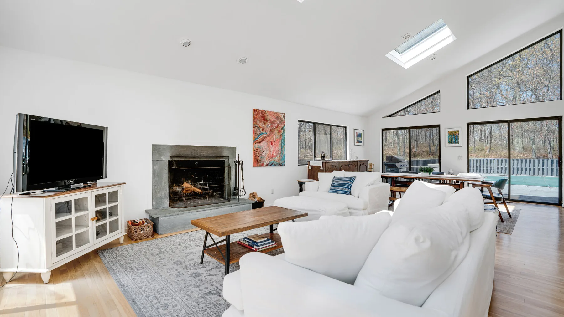 Una sala luminosa con asientos blancos, una chimenea y ventanas grandes.