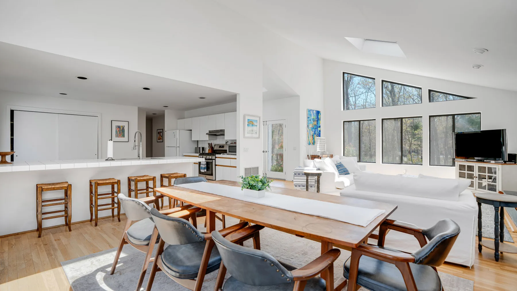 Una luminosa sala de estar y comedor de planta abierta con una larga mesa de madera y grandes ventanas.