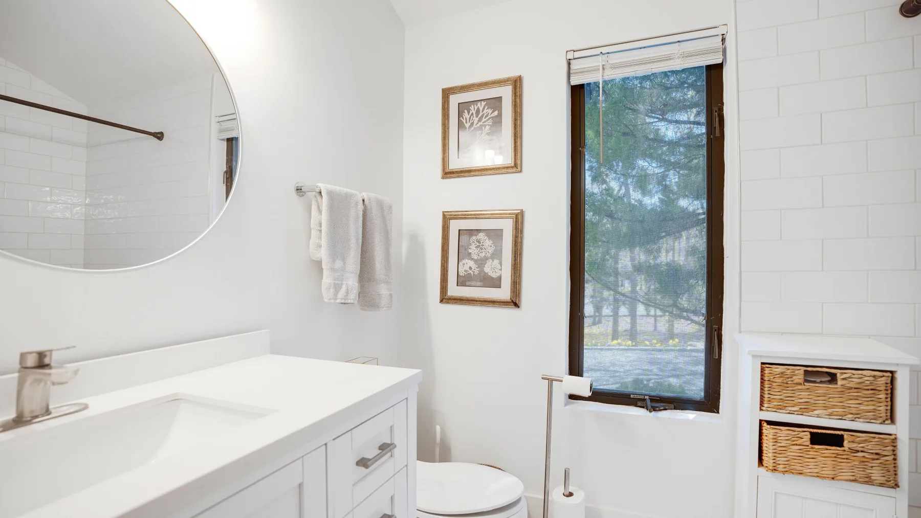A bright bathroom with a white vanity, toilet, and window.