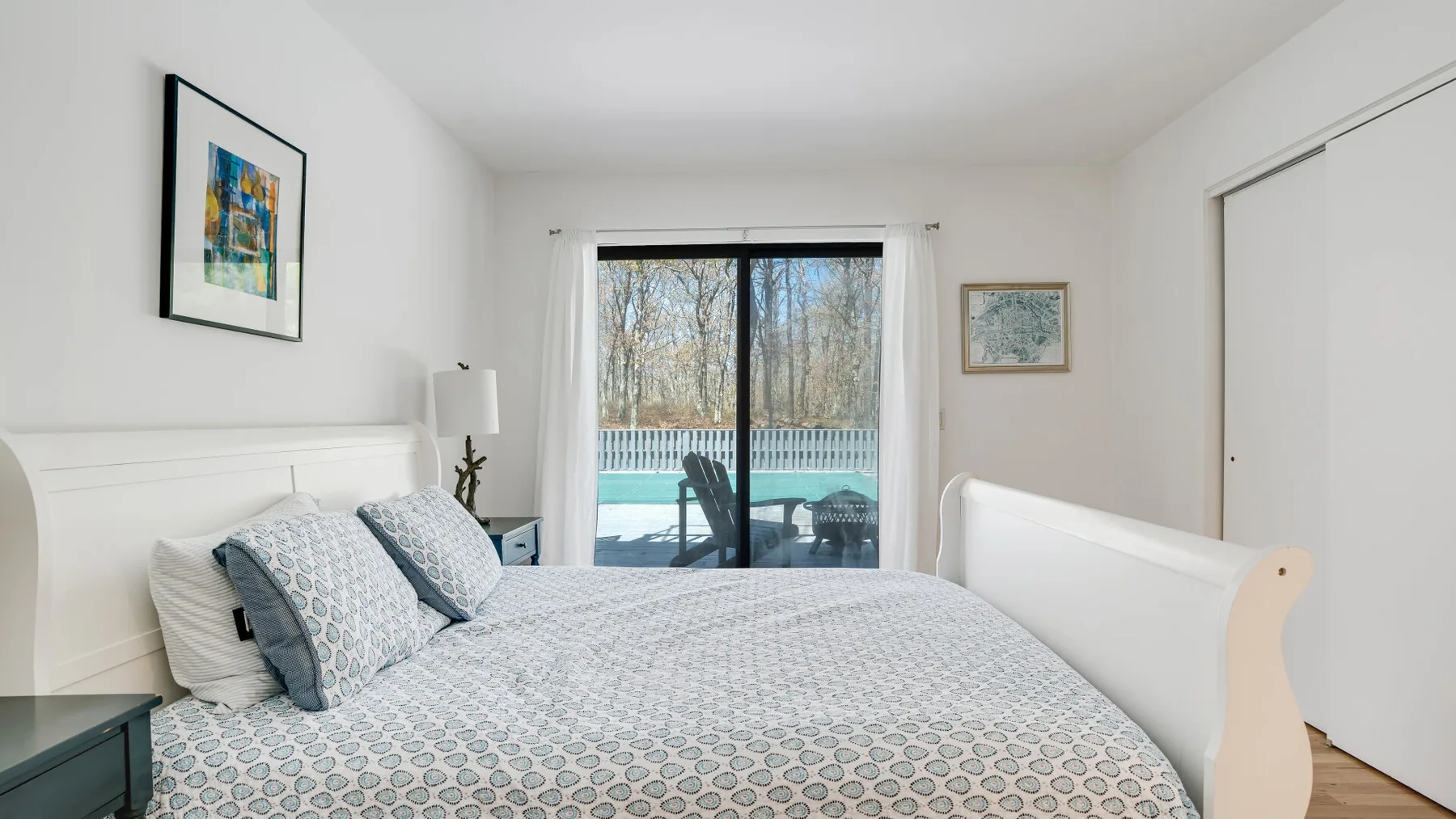 A bright bedroom with a bed beside sliding glass doors overlooking a pool.