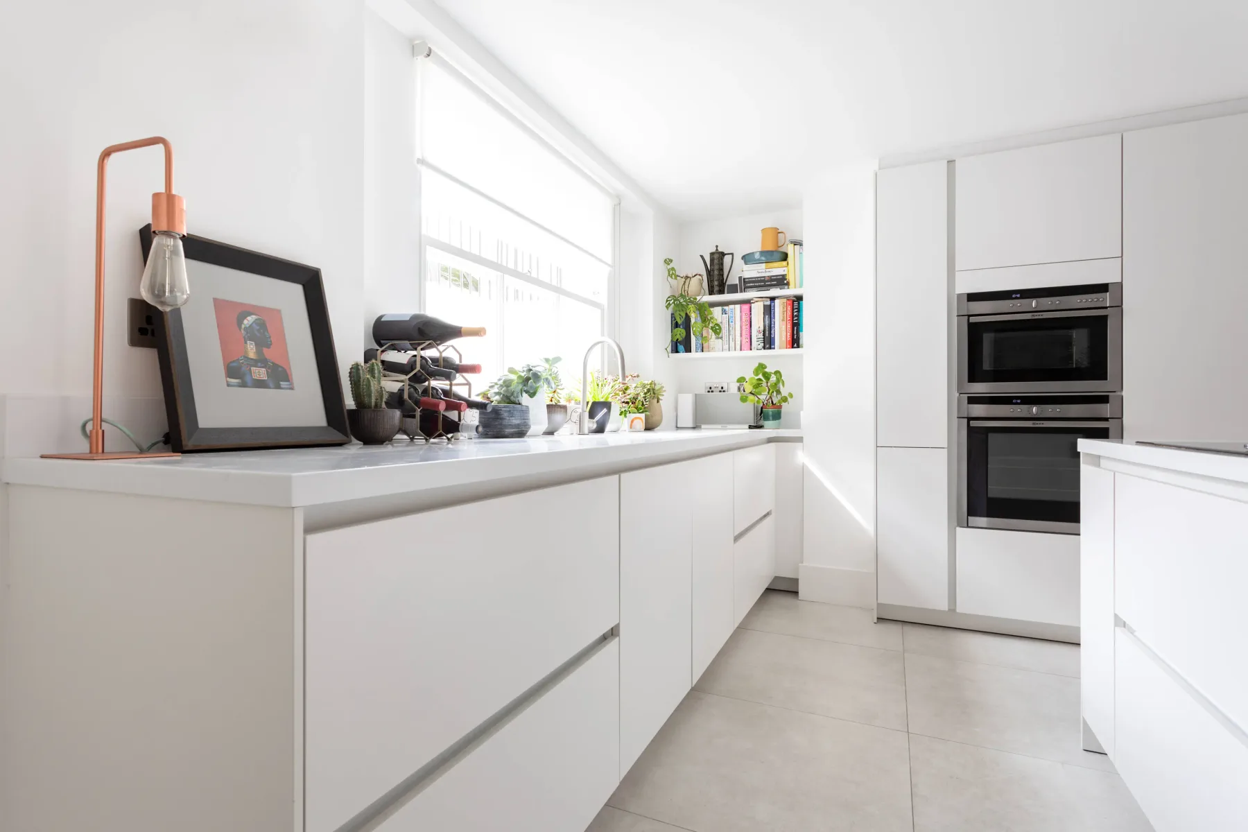 Una cocina moderna y luminosa tiene gabinetes blancos y una encimera larga bajo una ventana.