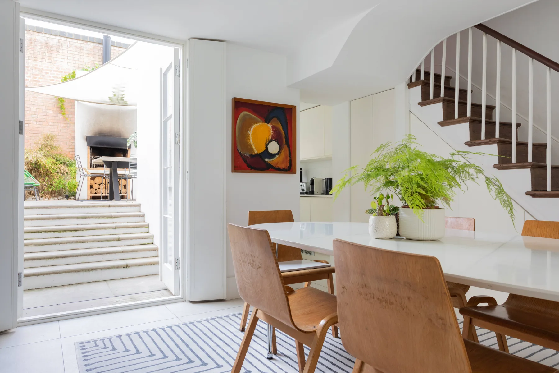 Un comedor luminoso con mesa, asientos y una escalera junto a una puerta abierta.
