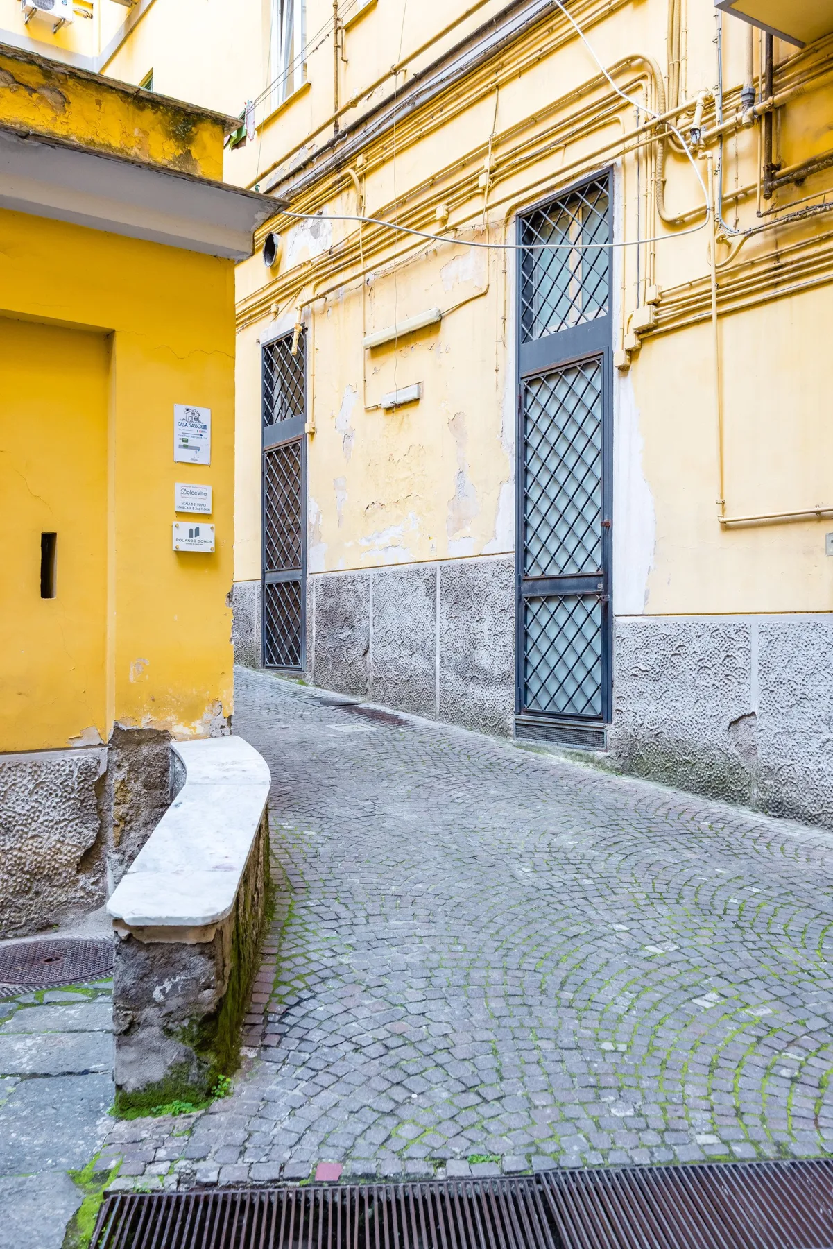 Un callejón estrecho adoquinado pasa entre edificios amarillos con portones metálicos.