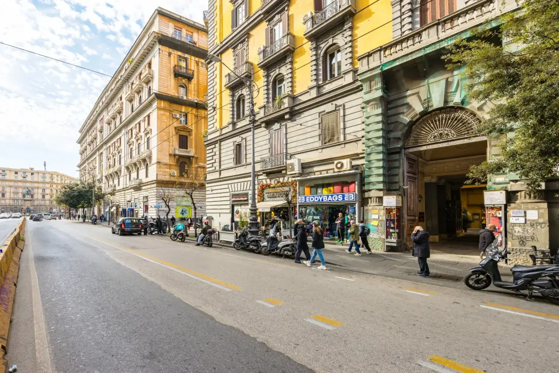 Una calle urbana flanqueada por edificios de varias plantas, comercios y scooters estacionados.