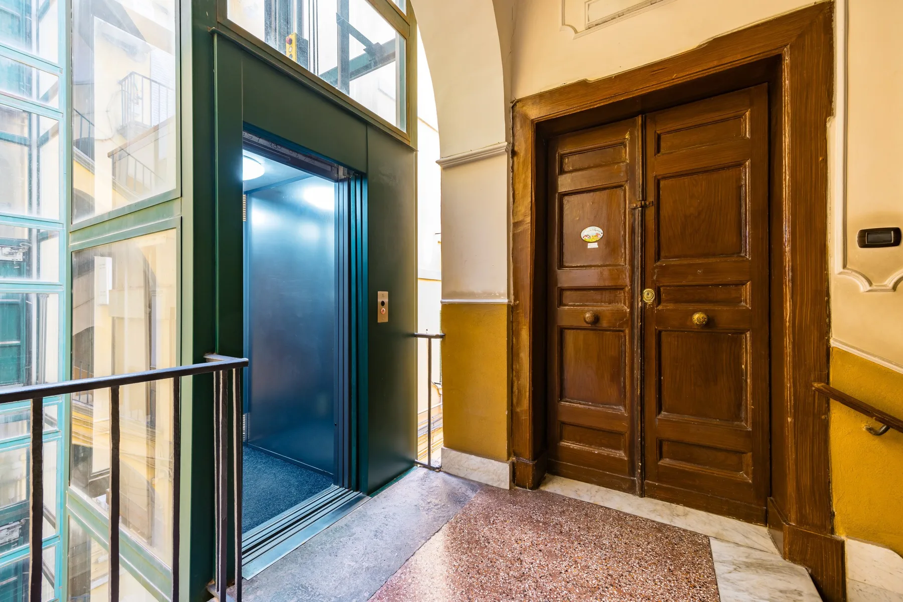 La entrada de un ascensor junto a una puerta doble de madera oscura en un pasillo iluminado.