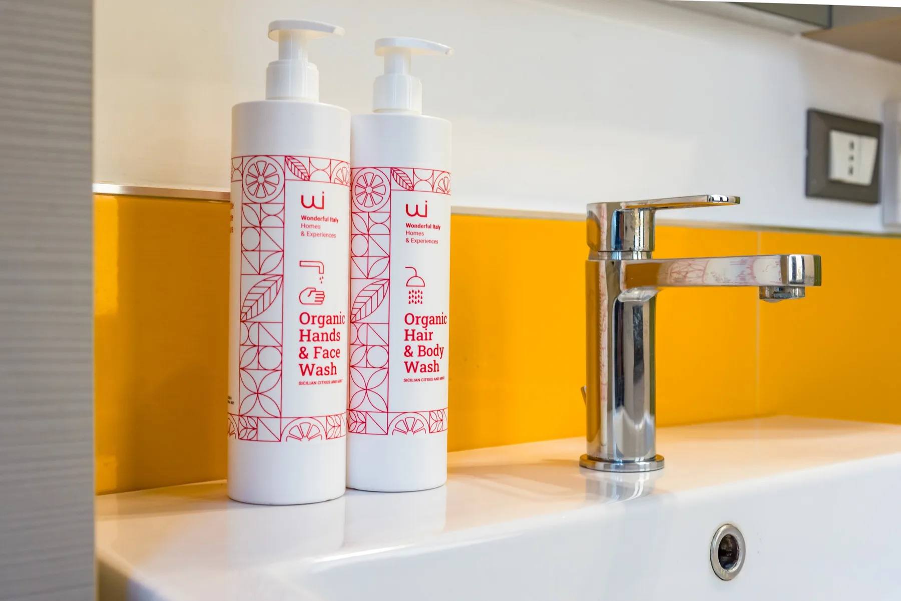 Un lavabo de baño con grifo cromado y dos dispensadores frente a un revestimiento amarillo.