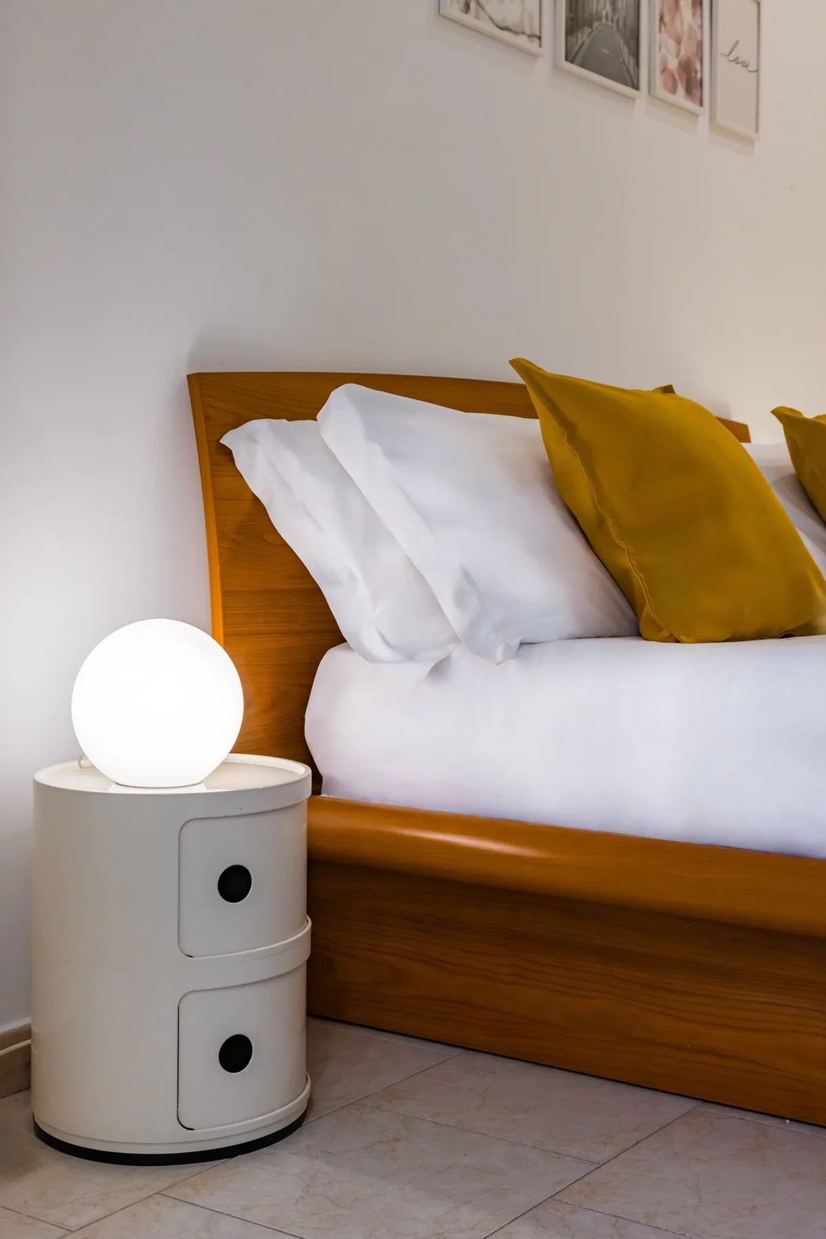 Un dormitorio con una cama de madera, ropa de cama blanca y una lámpara redonda junto a la cama.